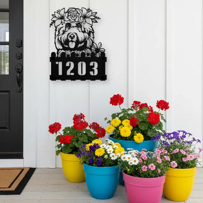 Cockapoo custom metal house number sign in black, flush mounted on white porch siding beside a black front door with colorful potted flowers