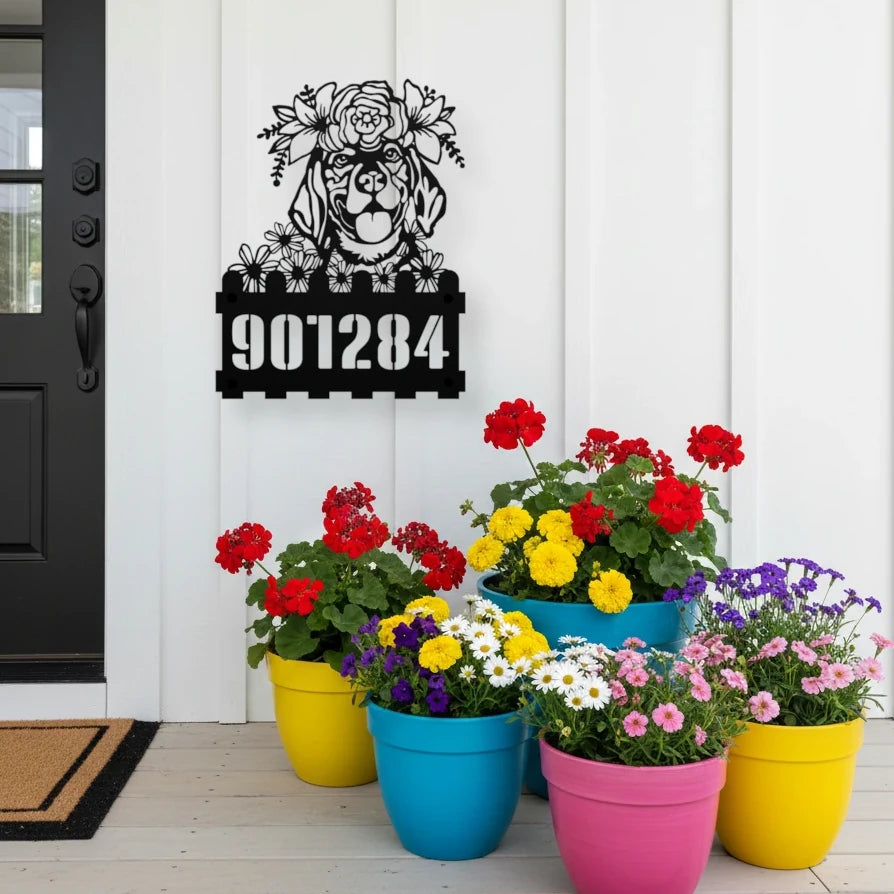 Beagle custom metal house number sign in black, flush mounted on white porch siding beside a black front door with colorful potted flowers