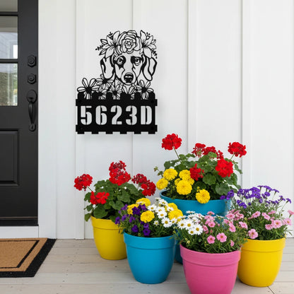 Dachshund custom metal house number sign in black, flush mounted on white porch siding beside a black front door with colorful potted flowers