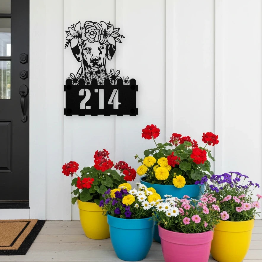 Dalmatian custom metal house number sign in black, flush mounted on white porch siding beside a black front door with colorful potted flowers