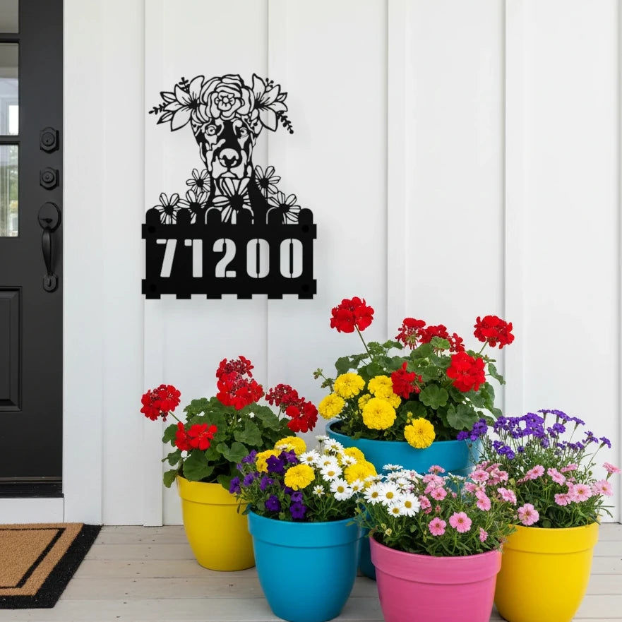Doberman custom metal house number sign in black, flush mounted on white porch siding beside a black front door with colorful potted flowers