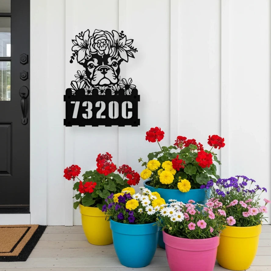 French Bulldog custom metal house number sign in black, flush mounted on white porch siding beside a black front door with colorful potted flowers