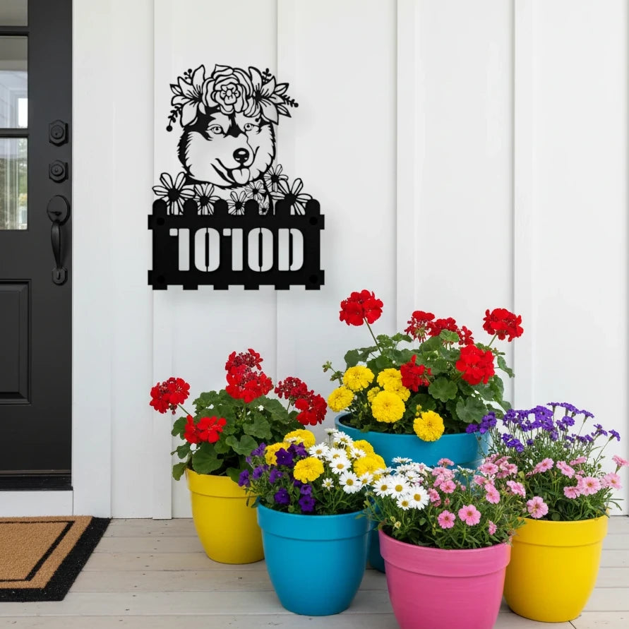 Husky custom metal house number sign in black, flush mounted on white porch siding beside a black front door with colorful potted flowers