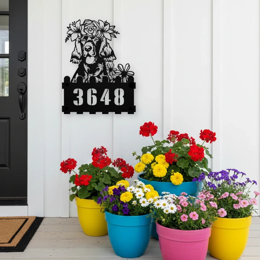 Irish Setter custom metal house number sign in black, flush mounted on white porch siding beside a black front door with colorful potted flowers