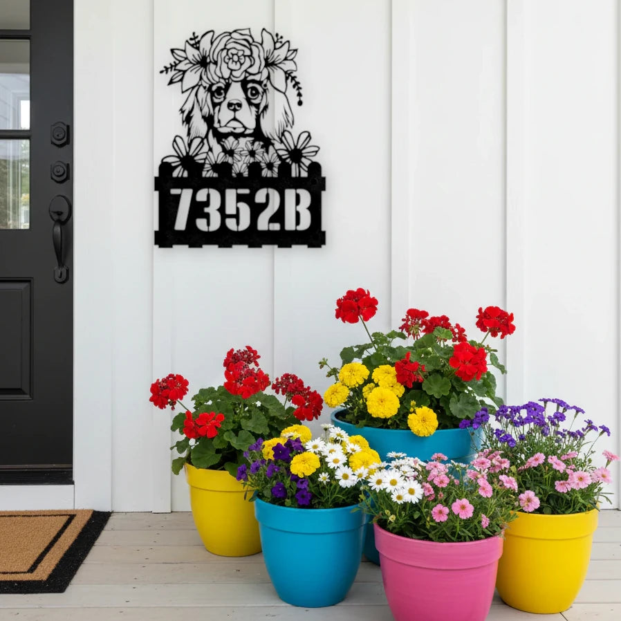 King Charles custom metal house number sign in black, flush mounted on white porch siding beside a black front door with colorful potted flowers