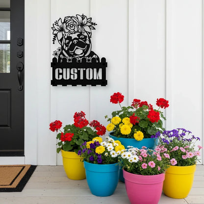 Pug custom metal house number sign in black, flush mounted on white porch siding beside a black front door with colorful potted flowers
