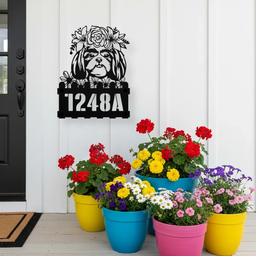 Shih Tzu custom metal house number sign in black, flush mounted on white porch siding beside a black front door with colorful potted flowers