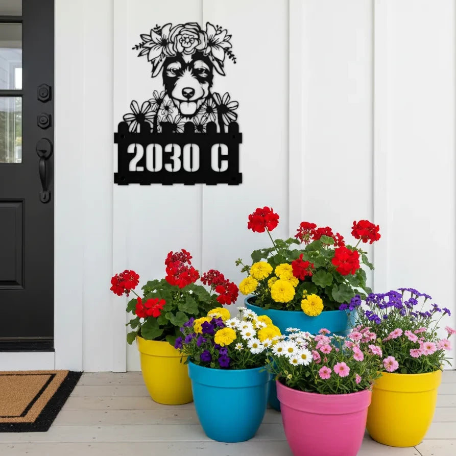 Jack Russell custom metal house number sign in black, flush mounted on white porch siding beside a black front door with colorful potted flowers