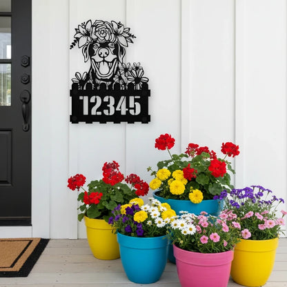 Labrador custom metal house number sign in black, flush mounted on white porch siding beside a black front door with colorful potted flowers