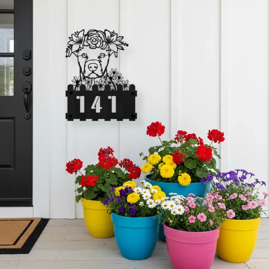 Pit Bull custom metal house number sign in black, flush mounted on white porch siding beside a black front door with colorful potted flowers