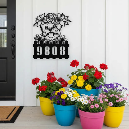 Yorkie custom metal house number sign in black, flush mounted on white porch siding beside a black front door with colorful potted flowers